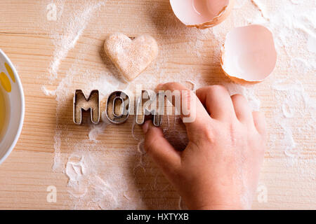 La fête des Mères, la composition. Faire des biscuits. Mains de méconnaissable girl holding emporte-pièce. Coeur de pâtisserie et coquilles d'œufs pondus sur table. Studio shot o Banque D'Images