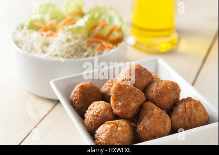 Tofu frit boules sur une plaque carrée blanche avec une salade verte et d'huile d'olive sur un fond de bois blanc Banque D'Images