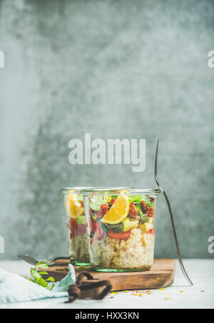 Salade saine avec quionoa, Avocat, tomates séchées, basilic, menthe, orange en bocaux sur planche de bois, mur gris à l'arrière-plan, selective focus, copie Banque D'Images