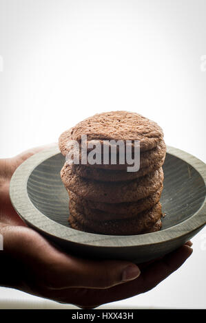 Pile de cookies Brownie dans un bol en bois gris sur mains modèle rétroéclairé shot Banque D'Images