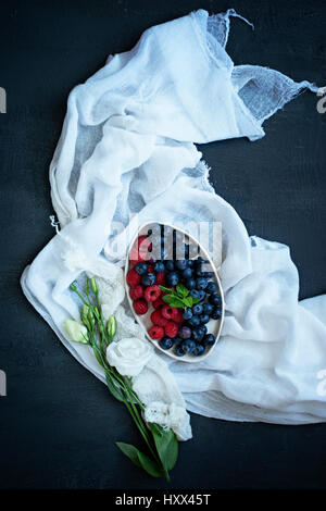 Un bol de fruits d'été sur le tissu blanc, avec des fleurs. Banque D'Images