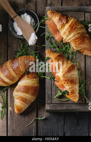 Un croissant avec du saumon salé, fumé et épinards servi avec roquette bol de fromage à la crème sur la vieille table en bois sombre. Vue d'en haut Banque D'Images