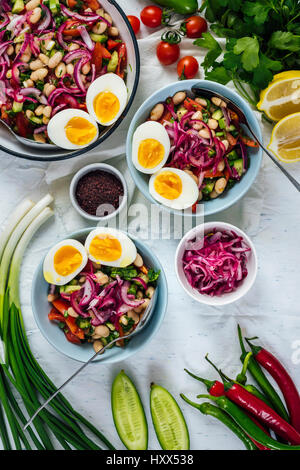 Salade de haricots piquante turc connu sous le piyaz servi dans des bols avec la moitié des œufs durs sur le dessus accompagné de sumac, oignons rouges, poivrons, oignon vert Banque D'Images