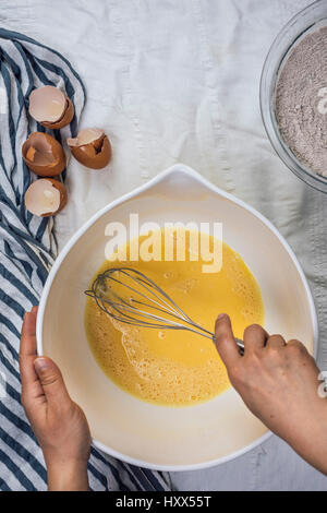 Une femme en fouettant les oeufs dans un grand bol, photographiés en vue de dessus. Coquilles d'œufs d'accompagner sur le côté. Banque D'Images