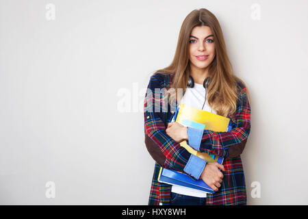 Portrait of young beautiful female student with books debout contre le mur. Banque D'Images