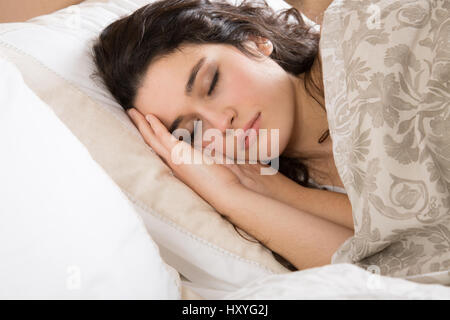 Jeune brunette woman sleeping in bed recouvert d'une courtepointe fleurie beige Banque D'Images