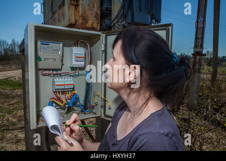 Technicien femme lecture pour vérifier le compteur d'électricité, la consommation d'électricité de puissance, debout près de l'appareillage de poste de transformation, à l'extérieur. Banque D'Images
