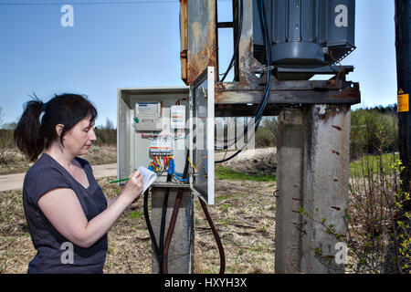 Femme technicien contrôle et de compteurs d'électricité, facture d'électricité de puissance, debout près de l'appareillage de poste de transformation, à l'extérieur. Banque D'Images