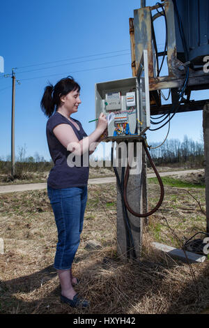 Contrôle de lecture de compteur électrique femme, debout près de l'appareillage électrique poste de transformation d'énergie, à l'extérieur. Banque D'Images