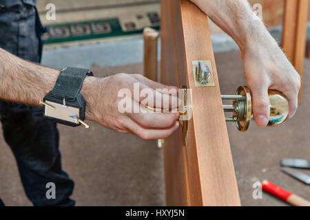 Installation de porte intérieure, un menuisier installe poignée avec un verrou dans le vantail à l'aide de vis de fixation pour bracelet magnétique, close-up. Banque D'Images