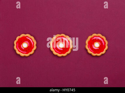 Trois biscuits en forme d'étoiles avec de la gelée rouge à l'intérieur se trouvent dans une ligne sur un fond marron Banque D'Images