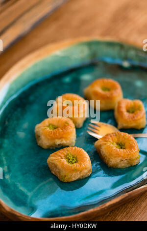 Six baklava à la pistache placés dans le bac en céramique turquoise avec la fourchette d'or mis sur table en bois Banque D'Images