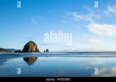 La belle mer Haystack Rock Pile est reflétée dans l'eau de la marée montante à Cannon Beach, Oregon Banque D'Images