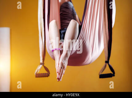 Young woman doing yoga anti-gravité position méditative en hamac au studio avec des murs jaunes Banque D'Images
