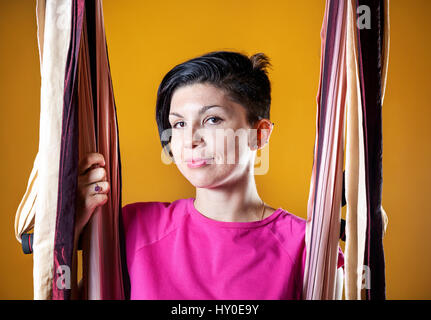 Portrait de jeune femme belle en hamac faisant l'antigravité au studio de yoga avec des murs jaunes Banque D'Images