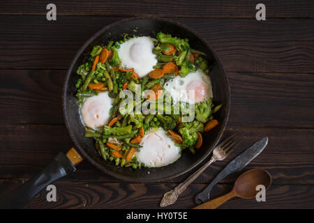 Poêlée de légumes et d'oeufs dans un poêlon sur table en bois foncé Banque D'Images