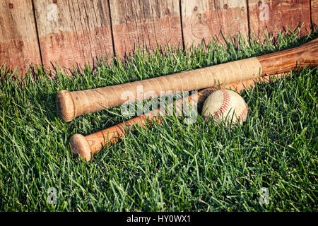 Vintage baseball et les chauves-souris se trouvant dans l'herbe en face d'une vieille clôture Banque D'Images