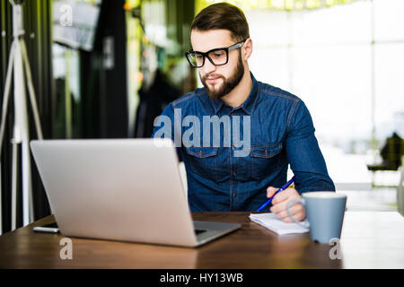Student taking notes de son nouvel ordinateur portable lors de la navigation sur Internet avec son café du matin Banque D'Images