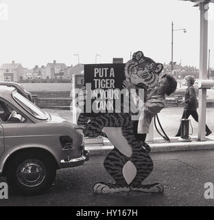 Années 1960, historique, dame tient une vente de garage avant-cour pour affichage carburant Esso, "mettre un tigre dans votre réservoir", en Angleterre. Visant à promouvoir le carburant Esso comme étant puissant, une bête dans votre moteur. Banque D'Images