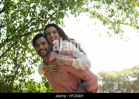 Low angle view of happy man piggybacking woman at park Banque D'Images