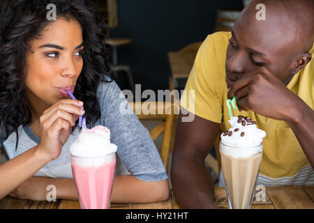 Jeune couple aimant avoir des milkshakes à table in coffee shop Banque D'Images