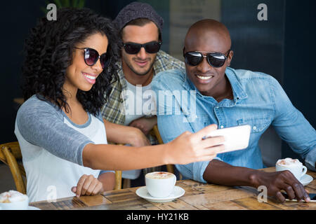 Happy multi ethnic friends portant des lunettes de soleil tout en prenant un café en selfies Banque D'Images