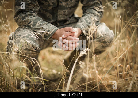 Soldat militaire accroupi dans l'herbe dans boot camp Banque D'Images
