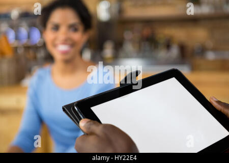 Image recadrée de barista hands holding digital tablet avec le client en arrière-plan de cafe Banque D'Images