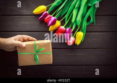 Bouquet de violet, rouge et jaune fleurs tulipes et la main de l'homme tenant une boîte-cadeau sur fond de bois. La femme ou la Fête des mères bonjour Banque D'Images