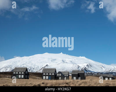 Une grappe de maisons noir est vu en face d'une montagne de neige dans l'ancien village de pêche de la péninsule de Snæfellsnes en 05960, l'Islande Banque D'Images