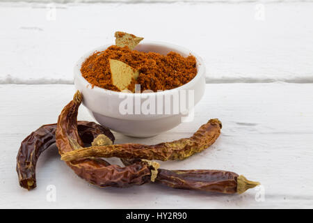 Piment rouge en poudre dans un bol blanc avec des piments séchés sur tableau blanc Banque D'Images