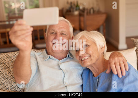 Smiling young couple cellphone autoportraits ensemble sur leur canapé Banque D'Images