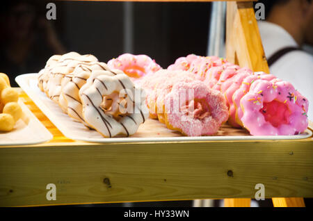 Affichage de délicieuses pâtisseries dans une boulangerie avec un assortiment de vitrages colorés et savoureux donuts ou beignets avec sprinkles et cerise sur des plateaux dans un pays de fabrication Banque D'Images