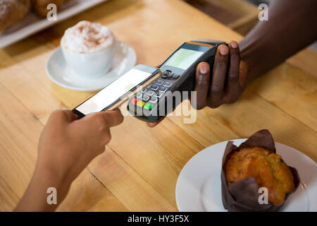 Image recadrée de barista acceptant le paiement par téléphone mobile au cafe Banque D'Images