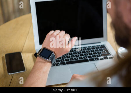 Portrait de jeune homme à l'aide de smart watch avec ordinateur portable et téléphone mobile sur table dans cafe Banque D'Images