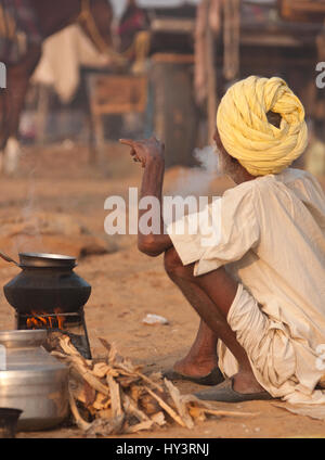 Vieil homme fumeurs à côté de son feu de camp à l'Assemblée Pushkar Foire de chameau au Rajasthan, en Inde. Banque D'Images