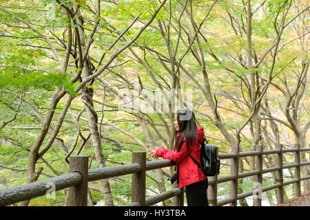 Touriste avec l'appareil photo en bandoulière et s'appuie sur la route en bois clôture en forêt avec les feuilles d'automne dans les gorges de Shosenkyo, Japon Banque D'Images