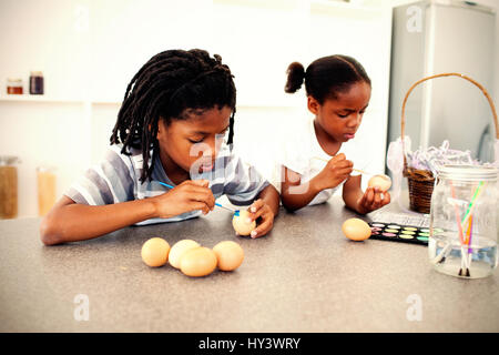 Frères et sœurs concentré dans la cuisine les oeufs de peinture Banque D'Images