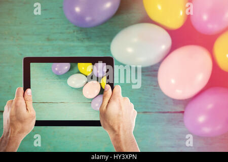 Cropped hand holding digital tablet contre diverses les oeufs de Pâques sur la surface en bois Banque D'Images