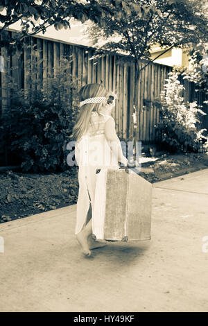 Little girl avec lacey dress transport des bagages loin comme si elle est un fugueur. Banque D'Images