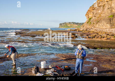 Hommes asiatiques mâles pêchant dans la roche à Bilgola Beach à Sydney, Nouvelle-Galles du Sud, Australie portant un gilet de sauvetage. Banque D'Images