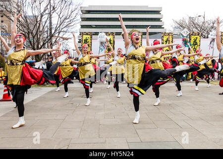 Danse Yosakoi Festival. Équipe de jeunes femmes danseurs, danser et chanter en face de bâtiment moderne. Porter un yukata jaune vestes. Banque D'Images