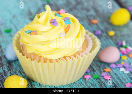 Cupcake de Pâques jaune avec des bonbons et saupoudre sur table en bois vintage Banque D'Images