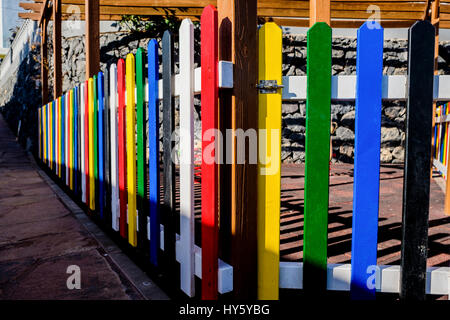 Coffre-fort aire de jeux entourée de poteaux de clôture en bois coloré peint en rouge, blanc, bleu, jaune, blanc et noir Banque D'Images