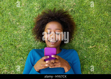 Portrait de dessus d'un smiling african woman lying on grass looking at cell phone Banque D'Images