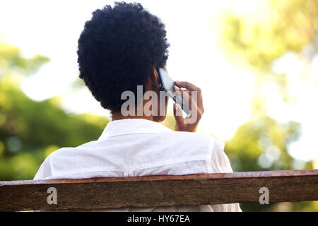 Portrait d'arrière jeune femme assise sur un banc de parc et talking on mobile phone Banque D'Images