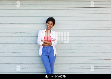 Portrait of a smiling young African woman with arms crossed standing contre un mur Banque D'Images