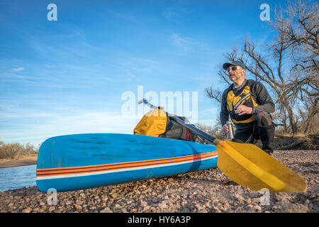 A senior male paddler est prendre du repos et pause thé sur un gravelbar au cours de Stand up Paddling sur la rivière South Platte, saison froide scenery Banque D'Images