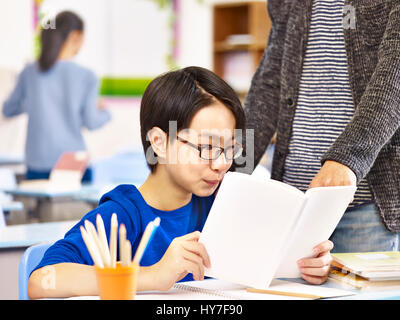 Écolier primaire asiatique obtenez de l'aide de professeur ou tuteur en classe à l'école. Banque D'Images