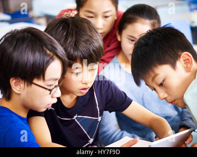 Groupe d'élèves des écoles primaires de l'Asie joue une partie de l'aide de tablet ensemble. Banque D'Images